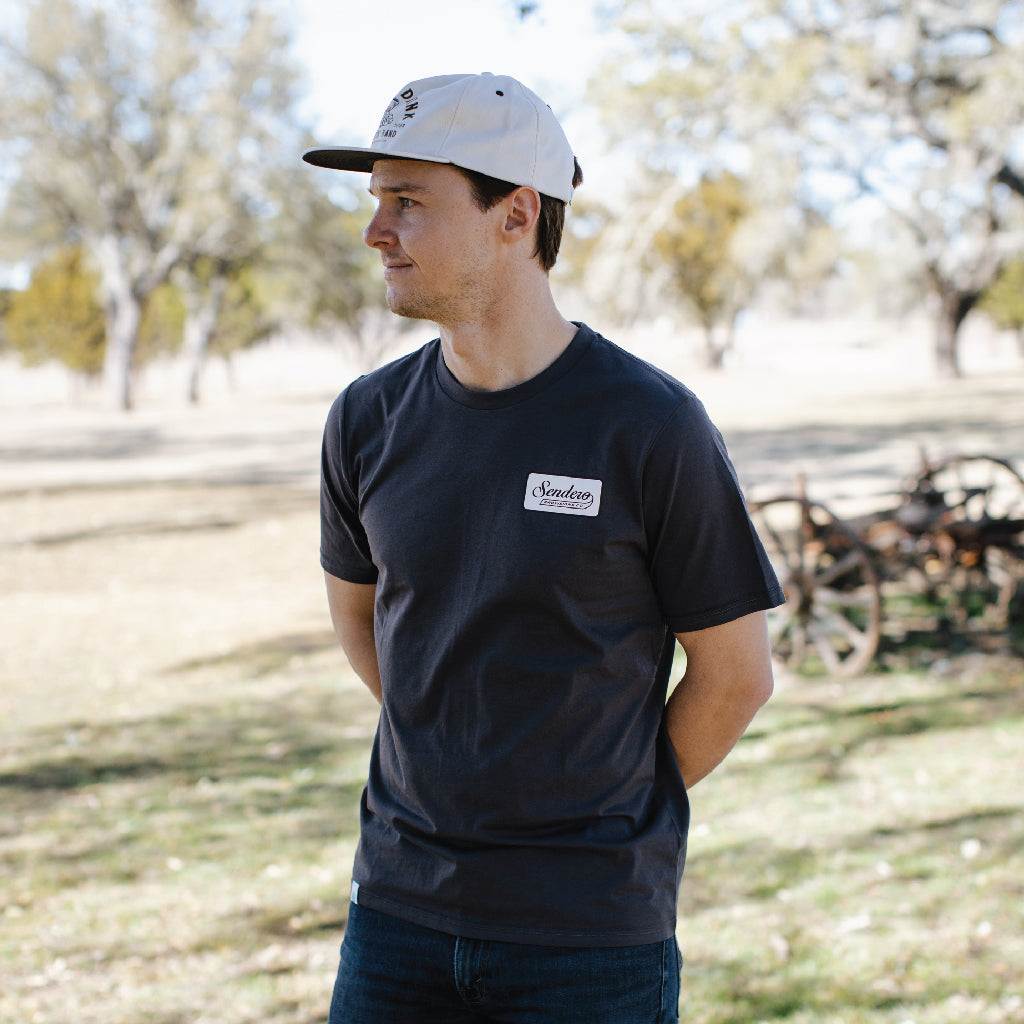 Man wearing Sendero Shootin' Hand cap, featuring screen printed design and durable cotton canvas, in outdoor setting.